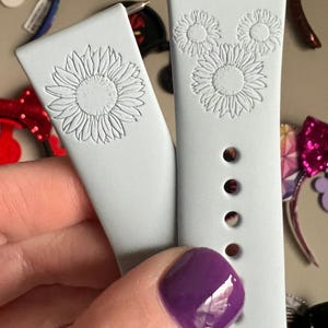 May include: Two light blue silicone watch bands with a white sunflower design. The band on the right has three sunflowers arranged in a Mickey Mouse shape.