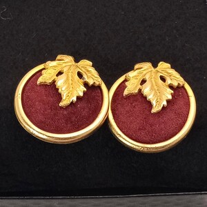 Puede incluir: Un par de pendientes de tono dorado con un centro de terciopelo burdeos y un diseño de hoja de oro.