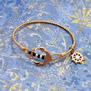 May include: A gold-toned bracelet with a twisted rope design. The bracelet features a black and white anchor charm and a gold-toned steering wheel charm.