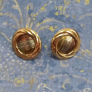 May include: A pair of gold-toned earrings with a circular design. The earrings have a textured, swirling pattern and a centre circle with a striped design.