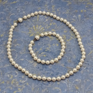May include: A set of white pearl jewellery, comprising a necklace and a bracelet. Both pieces are made of faux pearls and have gold-toned clasps.