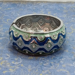 May include: A silver bangle bracelet with a blue and green geometric pattern and clear rhinestones.