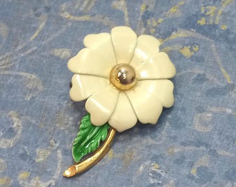 May include: A vintage flower brooch with a cream-colored enamel daisy design and a gold-tone center. The brooch features a green enamel leaf and a gold-tone stem, perfect for adding a touch of floral elegance to any outfit.