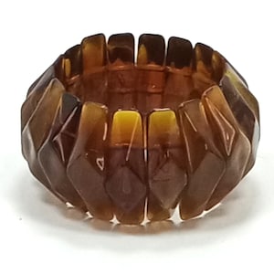 May include: A brown and amber colored plastic bracelet with a geometric design. The bracelet is made up of many small, interlocking pieces.