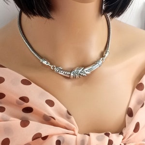 Op de afbeelding: Een zilveren choker ketting met een gedraaid, getextureerd ontwerp. De ketting is gemaakt van een dunne ketting en heeft een decoratieve sluiting.