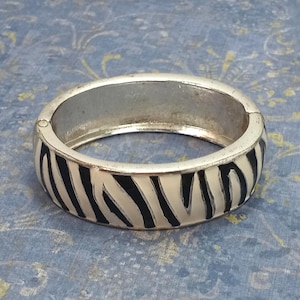 May include: A silver bangle bracelet with a black and white zebra print design.