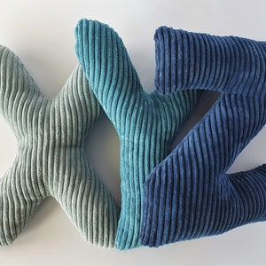 Op de afbeelding: Drie pluche kussens in de vorm van de letters X, Y en Z. Het X-kussen is licht saliegroen, het Y-kussen is blauwgroen en het Z-kussen is donker marineblauw. Elk letterkussen is gemaakt van een zachte, gestructureerde corduroy stof met verticale ribbels.