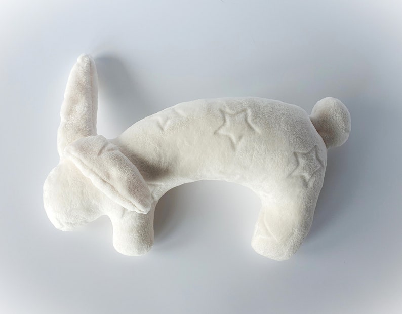 Puede incluir: Una almohada de cuello de peluche blanca con forma de conejo con bordados en forma de estrella.