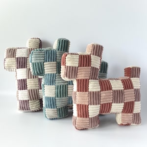 Può includere: Quattro cuscini a forma di cane in velluto a coste, nei toni del rosa, verde e beige. Ogni cuscino presenta un design patchwork, con un mix di pannelli di velluto a coste verticali e orizzontali. Su sfondo bianco.