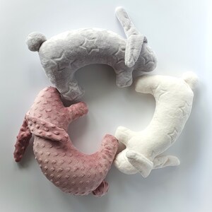 Puede incluir: Tres almohadas de peluche con forma de conejo dispuestas en c&iacute;rculo. Las almohadas son grises, blancas y rosas. La almohada gris tiene un patr&oacute;n de estrellas, la almohada blanca tiene un patr&oacute;n de estrellas y la almohada rosa tiene un patr&oacute;n de puntos.