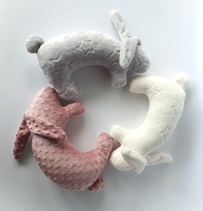 Puede incluir: Tres almohadas de peluche con forma de conejo dispuestas en c&iacute;rculo. Las almohadas son grises, blancas y rosas. La almohada gris tiene un patr&oacute;n de estrellas, la almohada blanca tiene un patr&oacute;n de estrellas y la almohada rosa tiene un patr&oacute;n de puntos.