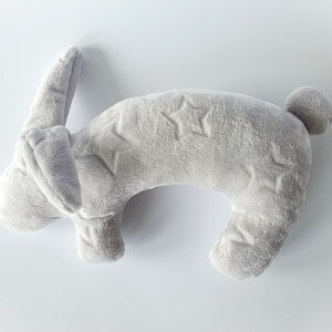 Puede incluir: Una almohada de cuello con forma de conejo de peluche gris con un patr&oacute;n de estrellas.
