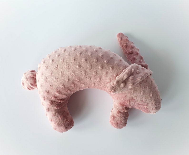 Puede incluir: Una almohada de peluche rosa en forma de conejo con una superficie texturizada. La almohada est&aacute; tumbada de lado con la cabeza girada hacia la derecha.