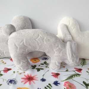 Puede incluir: Tres almohadas de felpa en forma de nube, coraz&oacute;n y conejo. Las almohadas son grises y blancas con un patr&oacute;n de estrellas. Las almohadas est&aacute;n sobre un fondo blanco con un patr&oacute;n floral.