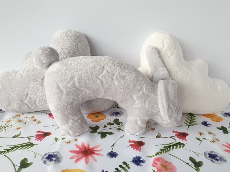 Puede incluir: Tres almohadas de felpa en forma de nube, coraz&oacute;n y conejo. Las almohadas son grises y blancas con un patr&oacute;n de estrellas. Las almohadas est&aacute;n sobre un fondo blanco con un patr&oacute;n floral.