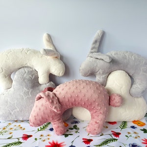 Puede incluir: Tres almohadas de peluche con forma de conejo en gris, blanco y rosa. Las almohadas est&aacute;n apiladas, con el conejo gris en la parte superior, el conejo blanco en el medio y el conejo rosa en la parte inferior. Las almohadas est&aacute;n hechas de un tejido suave y peludo y tienen un patr&oacute;n de estrellas.
