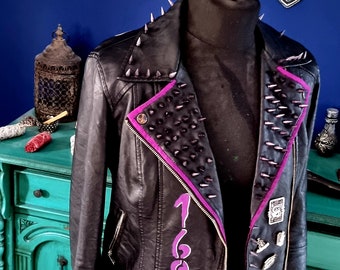 May include: Black leather jacket with purple accents and silver studs. The jacket has a zipper closure and a collar. The jacket has the number 1692 written on the front in purple.