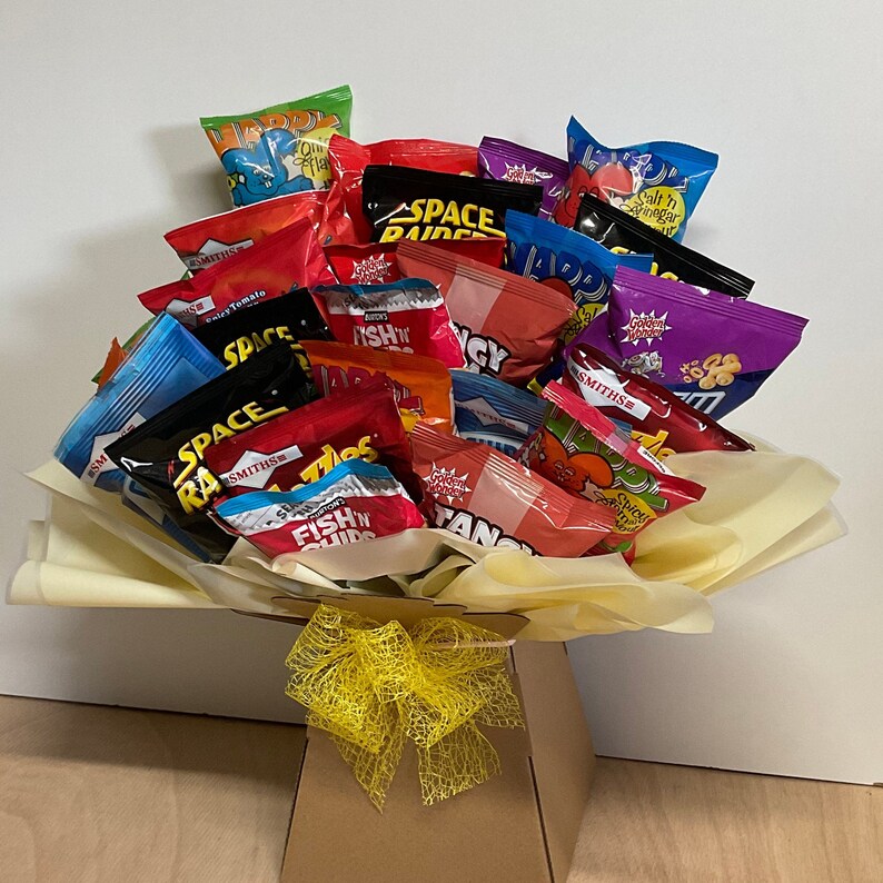 May include: A bouquet of various colorful chip bags, including brands like Smiths and Space Raiders, arranged in a decorative presentation. The arrangement is set in a cardboard box with a yellow bow, creating a unique gift.