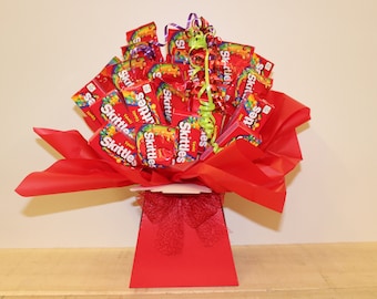 May include: A red gift basket filled with individually wrapped bags of Skittles candy. The basket is decorated with red tissue paper and a red ribbon.