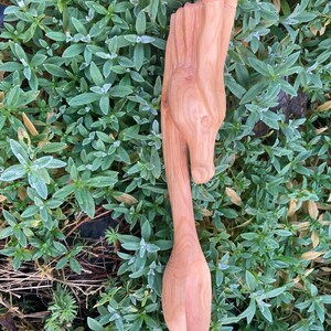 May include: A wooden spoon carved in the shape of a dragon's head. The spoon is a light brown color and has a smooth finish. The dragon's head is detailed with scales and a long snout.