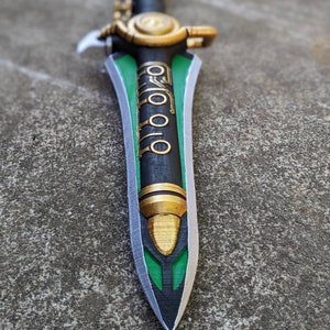Puede incluir: Una espada negra y verde con detalles dorados. La espada tiene un dise&ntilde;o decorativo en la hoja y una empu&ntilde;adura dorada.