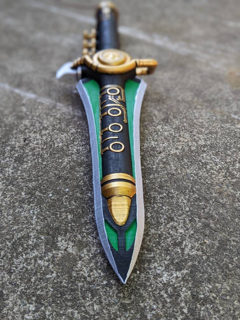 Puede incluir: Una espada negra y verde con detalles dorados. La espada tiene un dise&ntilde;o decorativo en la hoja y una empu&ntilde;adura dorada.