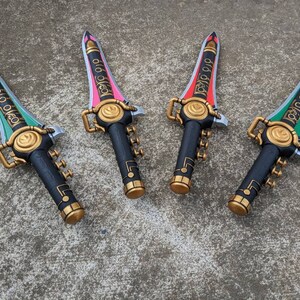 Puede incluir: Cuatro espadas de juguete de pl&aacute;stico negro con detalles dorados y hojas de diferentes colores. Las hojas son verdes, rosas, rojas y verdes. Las espadas tienen la palabra "Power Rangers" escrita en ellas.