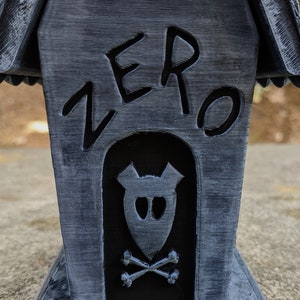 以下が含まれることがあります： 黒と灰色の犬小屋で、正面に「ZERO」と書かれています。犬小屋のドアにはドクロと交差した骨のデザインが施されています。