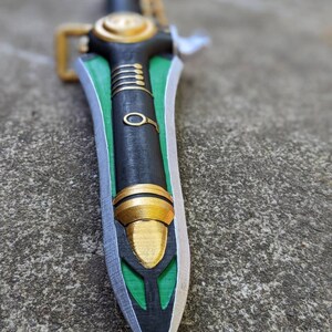 Puede incluir: Una espada negra y verde con detalles dorados. La espada tiene una punta afilada y un mango decorativo.