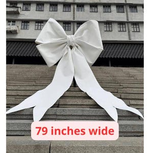 May include: A large white bow made of fabric, measuring 79 inches wide, is displayed on a set of concrete steps.