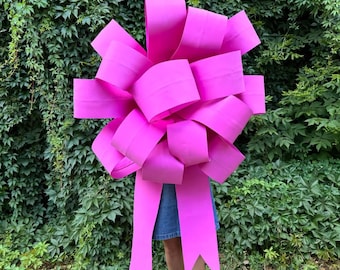 Op de afbeelding: Een grote, felroze strik gemaakt van papier. De strik is groot genoeg om de torso van een persoon te bedekken.