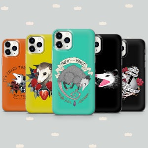 May include: A collection of five phone cases with opossum-themed designs. The cases are in various colors, including orange, yellow, and teal. Each case features a different illustration of an opossum, with text such as "Fake it till you make it."