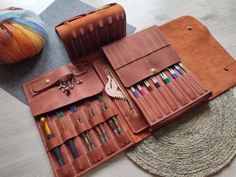 May include: A brown leather case with multiple compartments for storing knitting needles. The case is open and the needles are visible. The case has a zipper closure and a flap with a snap closure.
