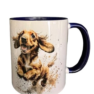 May include: White ceramic coffee mug with a blue rim and handle. The mug features a watercolor illustration of a brown and white dog with its tongue sticking out, running towards the right side of the mug.