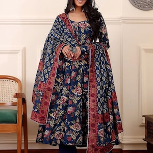May include: A navy blue floral print salwar kameez set. The set includes a long-sleeved tunic, matching pants, and a dupatta. The tunic and dupatta feature a red and white border. The floral pattern includes red and yellow flowers.