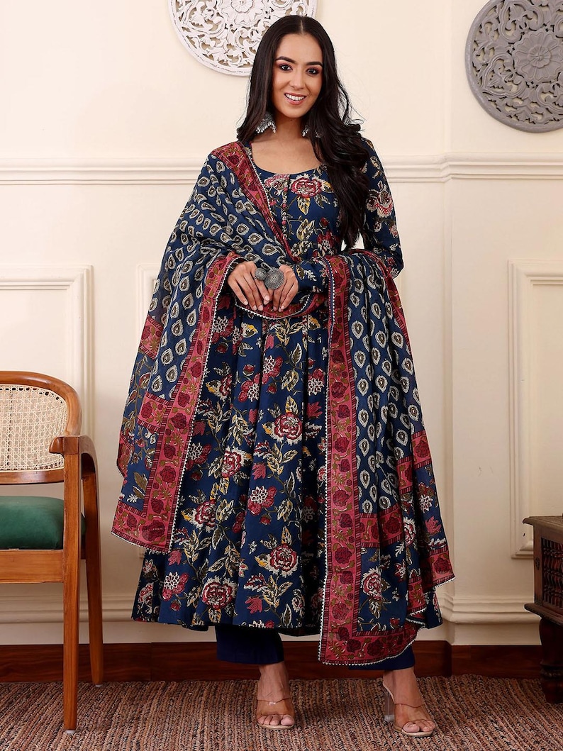 May include: A navy blue floral print salwar kameez set. The set includes a long-sleeved tunic, matching pants, and a dupatta. The tunic and dupatta feature a red and white border. The floral pattern includes red and yellow flowers.