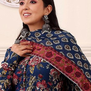 May include: A woman wearing a dark blue floral print dress with a matching scarf. The dress features a red and pink floral pattern. The scarf has a paisley design and a pink border. The woman is wearing silver earrings.