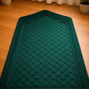May include: A dark teal prayer rug with a quilted diamond pattern. The rug has a decorative arched top and a border. The rug is on a wooden floor.