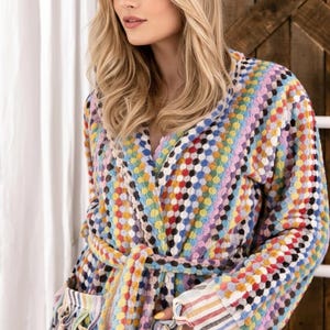 Pode incluir: Robe estampada multicolorida com cinto e bolsos. O robe apresenta uma mistura vibrante de cores, incluindo azul, amarelo, vermelho e roxo. As mangas e os bolsos têm um design listrado. O robe é feito de um material macio e texturizado.