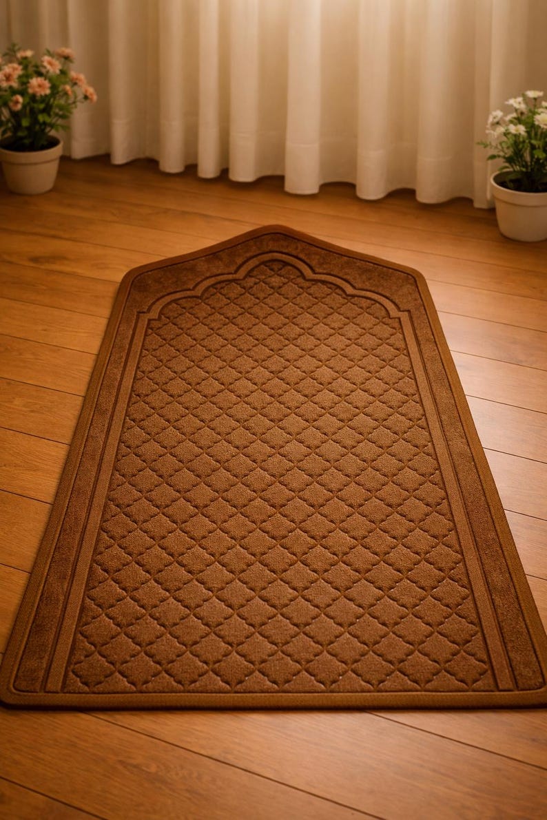 May include: A brown prayer rug with a diamond pattern and an arched top. The rug is rectangular with a decorative border. The rug is placed on a wooden floor.