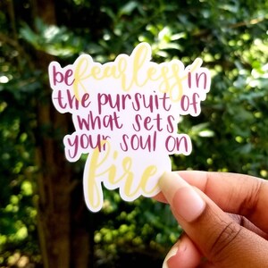 Könnte beinhalten: Ein weißer Aufkleber mit dem Text "be fearless in the pursuit of what sets your soul on fire" in gelber und burgunderfarbener Schrift.
