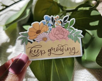 May include: A sticker with a floral design and the text "keep growing" in a cursive font. The flowers are pink, yellow, and blue.