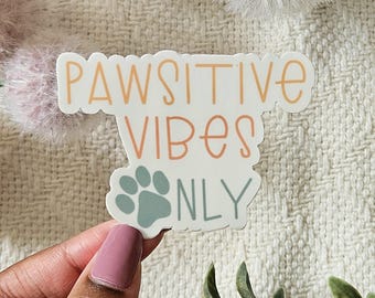 May include: A white sticker with the text "Pawsitive Vibes Only" in orange and green. A paw print is in the center of the sticker.