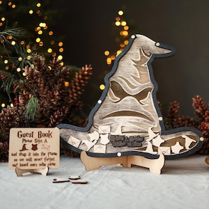 May include: Wooden Sorting Hat guest book with a sign that reads "Guest Book Please Sign A". The hat has a black border and is lit with small lights. Includes a stand and small wooden envelope cutouts. Three candles in wooden holders are in the foreground.