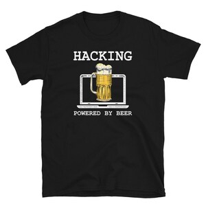 Puede incluir: Camiseta negra con texto blanco que dice "Hacking Powered by Beer". También hay una imagen de dibujos animados de una jarra de cerveza frente a una pantalla de computadora portátil en la camiseta.