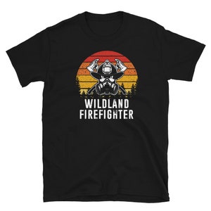 May include: Black t-shirt with a retro sunset graphic and a firefighter wearing a helmet and respirator. The text "Wildland Firefighter" is printed below the graphic.