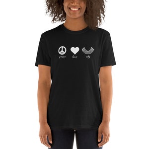 Puede incluir: Camiseta negra con un símbolo de paz blanco, un corazón y el texto "peace love rbg".