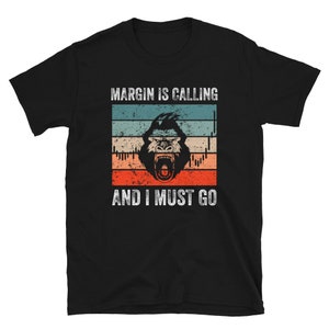 May include: Black t-shirt with a vintage-style graphic of a gorilla with a red, white, and blue background. The text "MARGIN IS CALLING AND I MUST GO" is printed on the shirt.