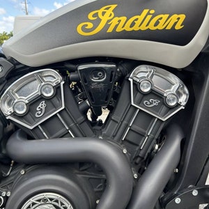 Puede incluir: Primer plano de un motor de motocicleta negro y plateado con la palabra "Indian" en letras amarillas en el tanque de gasolina.