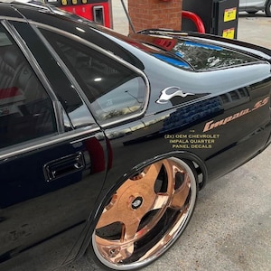 Peut inclure: Chevrolet Impala SS noire avec des jantes dorées et le texte "(2X) OEM CHEVROLET IMPALA QUARTER PANEL DECALS" sur le panneau arrière.